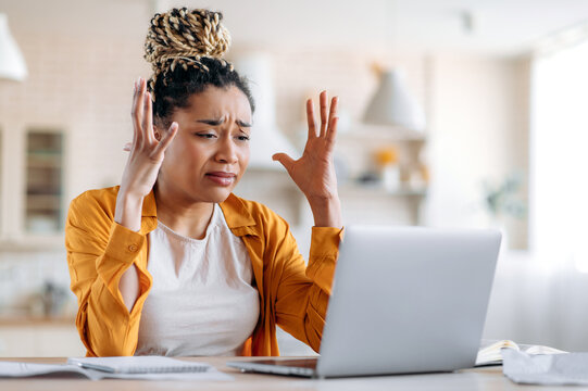 Tense indignant frustrated african american girl with dreadlocks, business woman, manager or freelancer working remotely at a laptop, experiencing stress at work, got bad message, gesturing with hands