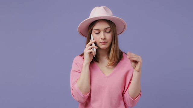 Irritated blonde young woman 20s years old in pink t-shirt hat isolated on violet purple background studio. People lifestyle concept. Talking on mobile phone showing blah blah gesture ja jaja hands