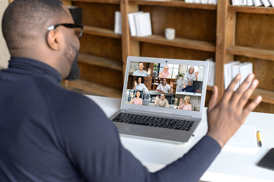 Back view of african businessman talk with co-workers partners using video call on laptop, discuss work project online, talking with clients, speak on webcam conference on computer, greeting