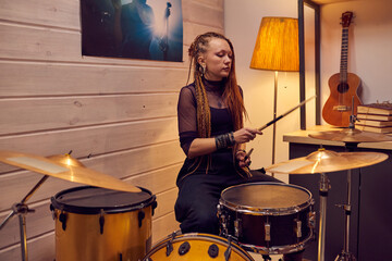 Fototapeta na wymiar Young female drummer holding sticks and playing drums during rehearsal in the studio