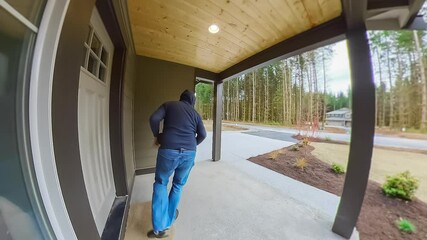 Package thief caught on home security camera in hoodie, sunglasses and face mask stealing a parcel from the porch of an American suburban house