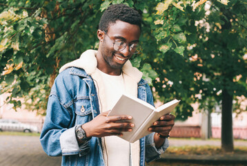 Portrait of young african man student reading a book wearing an eyeglasses in autumn city park