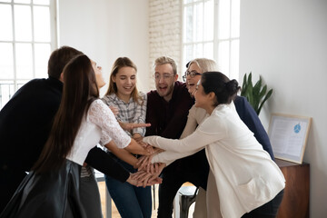 Overjoyed multiethnic businesspeople join stack hands in pile involved in teambuilding activity in office. Happy diverse multiracial colleagues coworkers participate in team training at meeting.