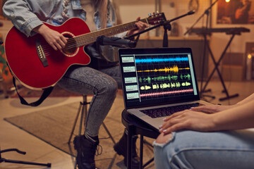 Close-up of woman using laptop and recording a song while musician playing guitar in the background in studio