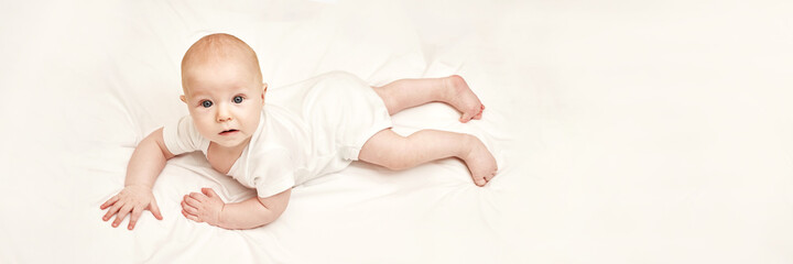 Cute small boy lying at bed. Childhood concept. Light background. Serious child. Copyspace. Stay home. Mockup. Horizontal banner. White clothes