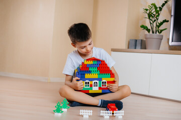 A little boy plays with a construction kit and builds a big house for the whole family. Construction of a family home.
