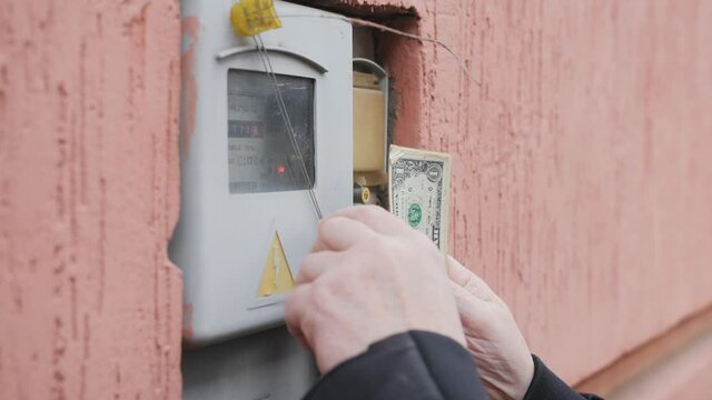 A man counts small bills against the background of an electricity meter. The concept of increasing the price of utility tariffs.