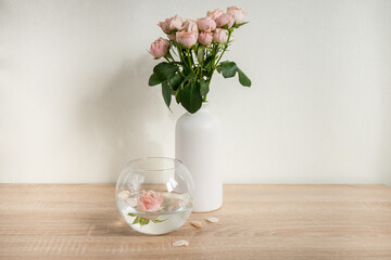 Portrait white picture frame mockup on wooden table. Modern ceramic vase with roses. White wall background. Scandinavian interior. 
