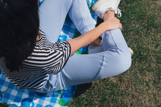 Young, Caucasian Woman Sitting On Picnic Mat With Blue White Gingham And Cherry Pattern. Top View With Copy Space.