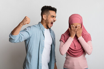 Domestic Violence Concept. Abusive arab husband threatening his crying wife in hijab