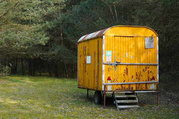 Old yellow rusty construction camper, trailer, van or wagon in the forest. Temporary housing for forest workers.