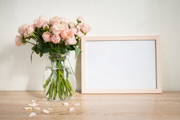 Portrait white picture frame mockup on wooden table. Modern glass vase with roses. White wall...