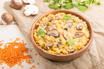Lentils porridge with champignons. and coriander in a wooden bowl on a white wooden background. Side view, selective focus.