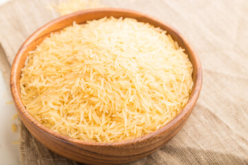 Wooden bowl with raw golden rice and wooden spoon on a white wooden background. Side view, selective focus.