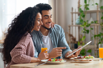 Fototapeta na wymiar Young Arab Couple Using Digital Tablet In Kitchen While Having Breakfast