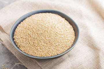 Blue ceramic bowl with raw white quinoa seeds on a gray concrete  background. Side view, selective focus.