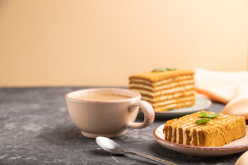Homemade honey cake with milk cream and mint with cup of coffee on a black and orange background. Side view, copy space.