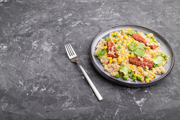 Quinoa porridge with green pea, corn and dried tomatoes on ceramic plate on a gray concrete background. Side view, copy space.