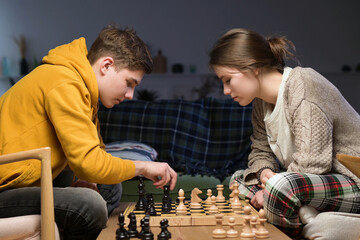 Young novice chess players play at home. Couple learning to play chess