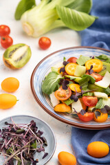 Vegetarian salad of pac choi cabbage, kiwi, tomatoes, kumquat, microgreen sprouts on a white concrete background. Side view, selective focus.