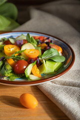 Vegetarian salad of pac choi cabbage, kiwi, tomatoes, kumquat, microgreen sprouts on a wooden background. Side view, close up, hard light, selective focus.