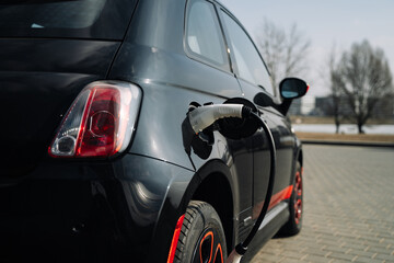A compact black electric car charges up in a parking lot to maintain the environment.
