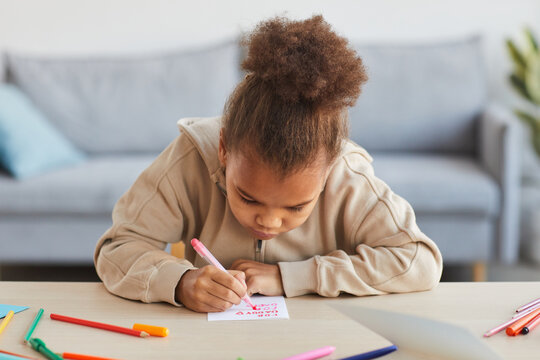 Front view portrait of cute African-American girl signing handmade card as gift for Fathers day, copy space