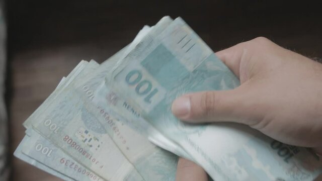 A close up shot of a man holding and counting money banknotes of Brazilian Real