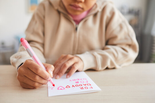 Close up of cute African-American girl signing handmade card as gift for Fathers day, copy space