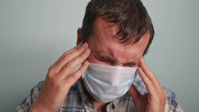 man wear puts on protective mask sick man feels pain in the head stress state a indoor portrait. epidemic corona outbreak concept. adult male face of sad tired in blue medical mask isolated