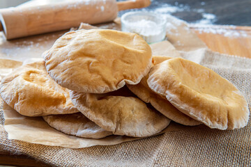 Stack of homemade, fluffy, pita bread. Freshly baked gluten-free pita bread on a rustic cloth, hot from the oven. Round flatbread that can be stuffed with food. Rolling pin and flour in the background