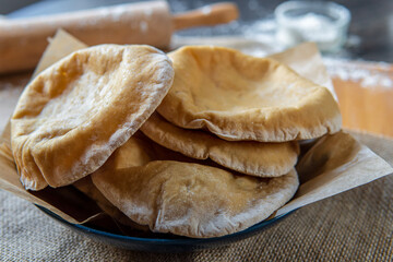 Stack of homemade, fluffy, pita bread. Freshly baked gluten-free pita bread on a rustic cloth, hot from the oven. Round flatbread that can be stuffed with food. Rolling pin and flour in the background