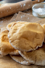 Stack of homemade, fluffy, pita bread. Freshly baked gluten-free pita bread on a rustic cloth, hot from the oven. Round flatbread that can be stuffed with food. Rolling pin and flour in the background