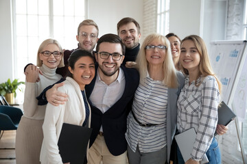 Portrait of overjoyed multiracial businesspeople have fun hug and embrace show unity at workplace. Happy diverse multiethnic colleagues coworkers look at camera feel motivated. Teamwork concept.