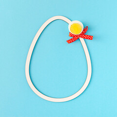 2021 Easter unique composition made of white egg frame, peace of boiled egg and red ribbon. Minimal holiday concept on pastel blue background. Flat lay.