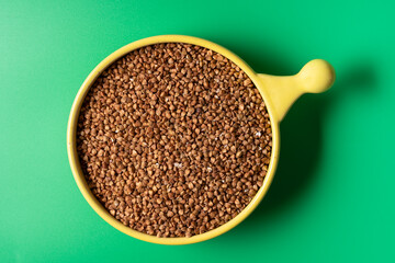 Top view of buckwheat in a bowl over green background, with copy space.