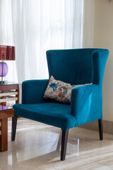 Teal soft vintage armchair, vertical orientation. Turquoise velvet armchair next to the window in the living room