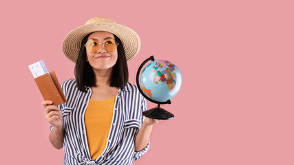 Dreamy asian woman holding passport with boarding pass and globe