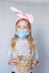 blonde girl in a striped jacket, on a bright background, with rabbit ears on her head, holding a basket of eggs, smiling in a medical mask