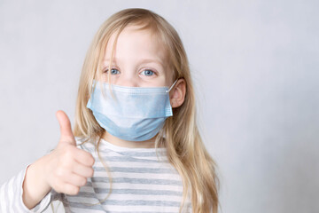 Blonde girl in striped jacket and medical mask removes holds finger thumb up