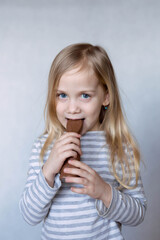 Blonde girl in striped jacket on a light background bites chocolate hare in front of her face smiles