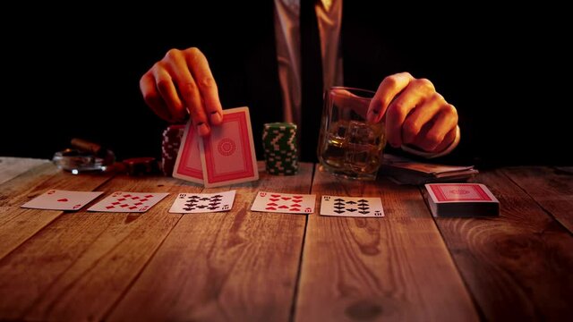 Man playing poker is waiting for his turn with glass full of whisky and two cards in his hands. He throws aces on the table and drinks alcohol. Concept of hazard games. Person in a suit rests in a bar