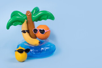 Creative fun idea with a banana, orange and lemon in sunglasses lying on a palm tree inflatable ring on a blue background.