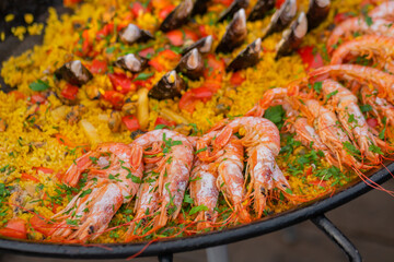 Close up: cooked yellow paella with shrimp, mussel, rice, spice, saffron in huge paella pan at summer outdoor food market. Spanish cuisine, seafood, gastronomy, street food concept