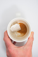 Mano de hombre cogiendo una taza de té con azúcar moreno para preparar una infusión estimulante.