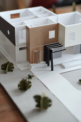 Obraz na płótnie Canvas Model of paper house and yard with green trees standing on workplace of contemporary architect or engineer in front of camera in office