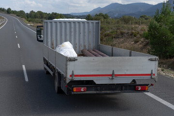 Un camión pequeño con la caja descubierta que transporta mercancías por carretera subiendo un...