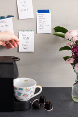 Woman hand holding the coffee reminder note from a grey wooden wall full of sticky notes next to a...
