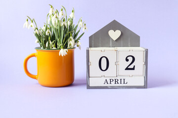Calendar for April 2: cubes with the numbers 0 and 2, the name of the month of April in English, a bouquet of snowdrops in a yellow tea mug on a blue background