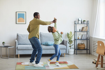 Full length portrait of happy African-American father dancing with daughter while having fun in...